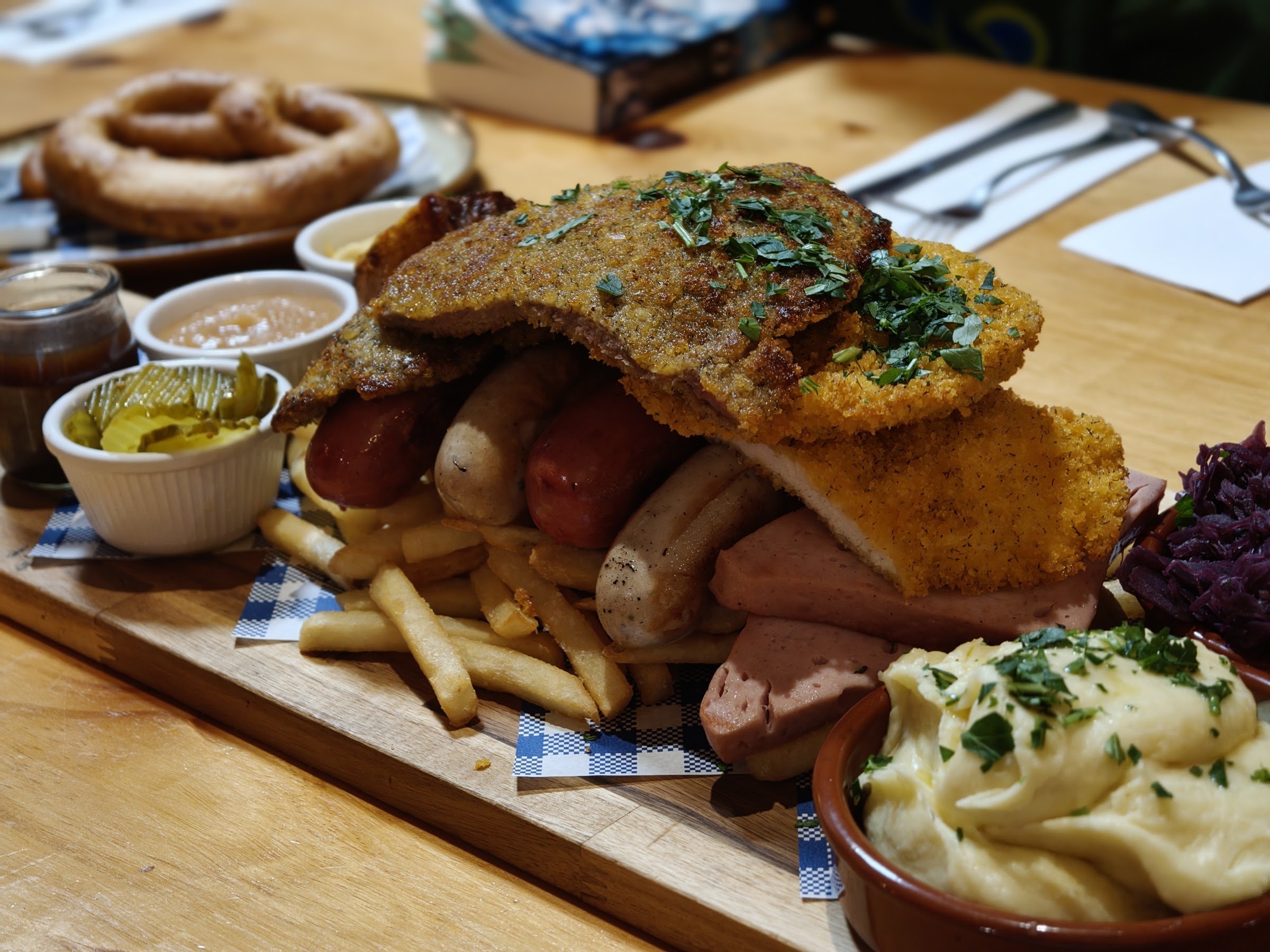 A German platter of schnitzel, sausages, pretzel, mash and sauerkraut on a wooden board